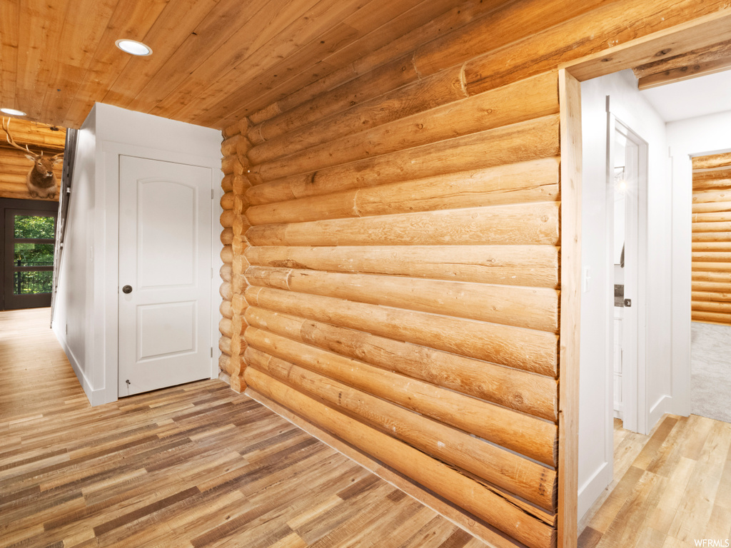 Hall with light hardwood flooring, wood ceiling, and log walls
