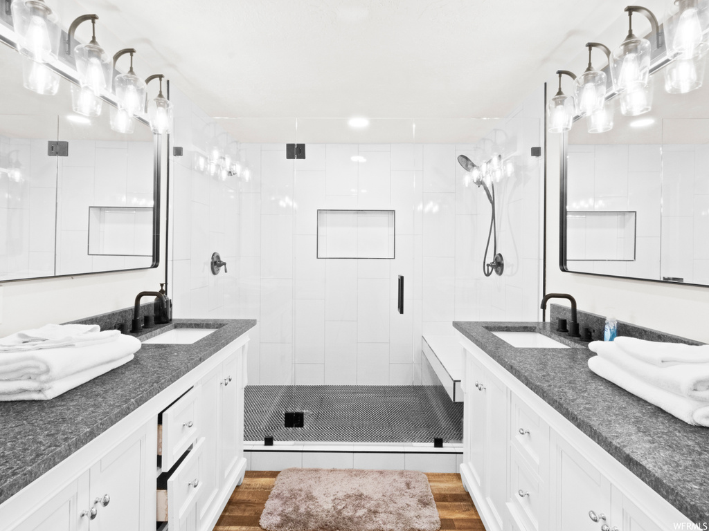 Bathroom with double vanity, a shower with shower door, mirror, and hardwood flooring