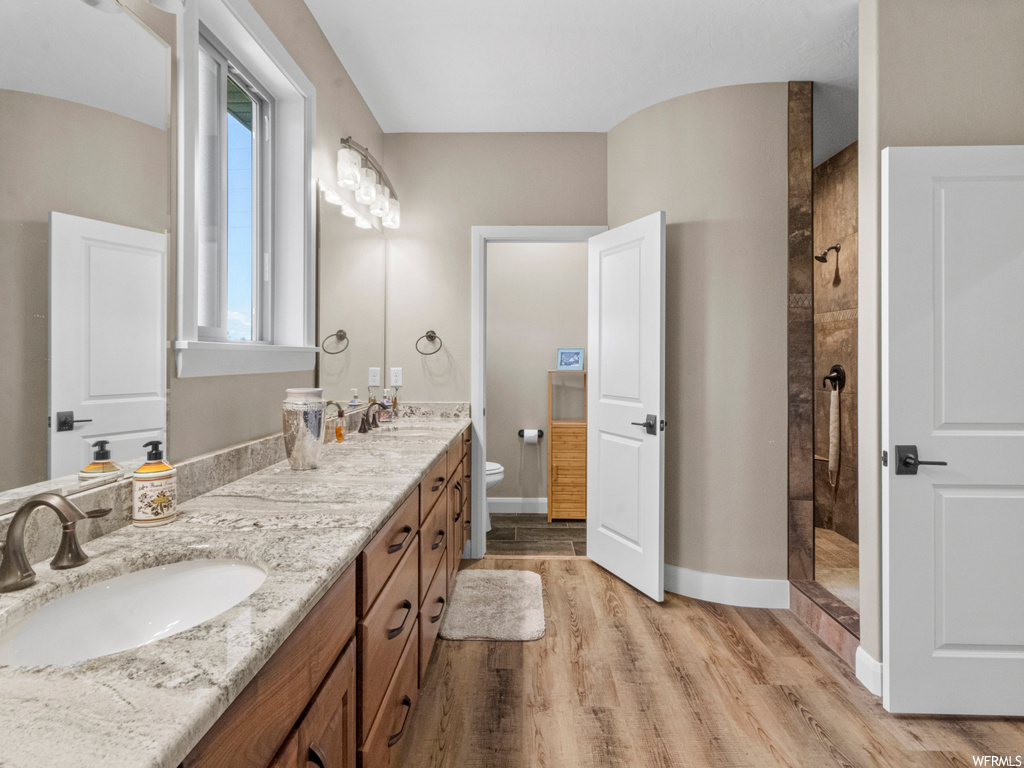 Bathroom featuring dual bowl vanity, a tile shower, mirror, and light hardwood flooring