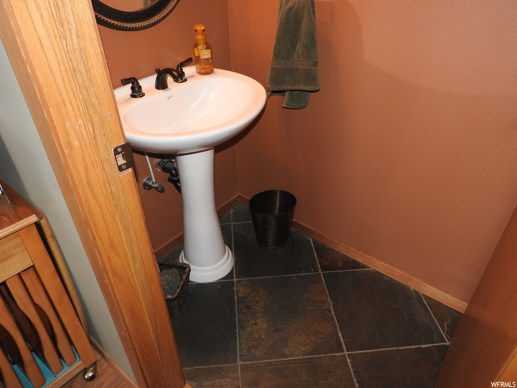 Bathroom featuring washbasin, mirror, and dark tile flooring