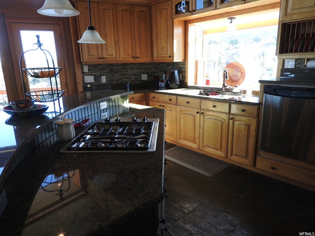 Kitchen featuring stainless steel dishwasher, decorative light fixtures, backsplash, black gas cooktop, dark tile flooring, and dark countertops