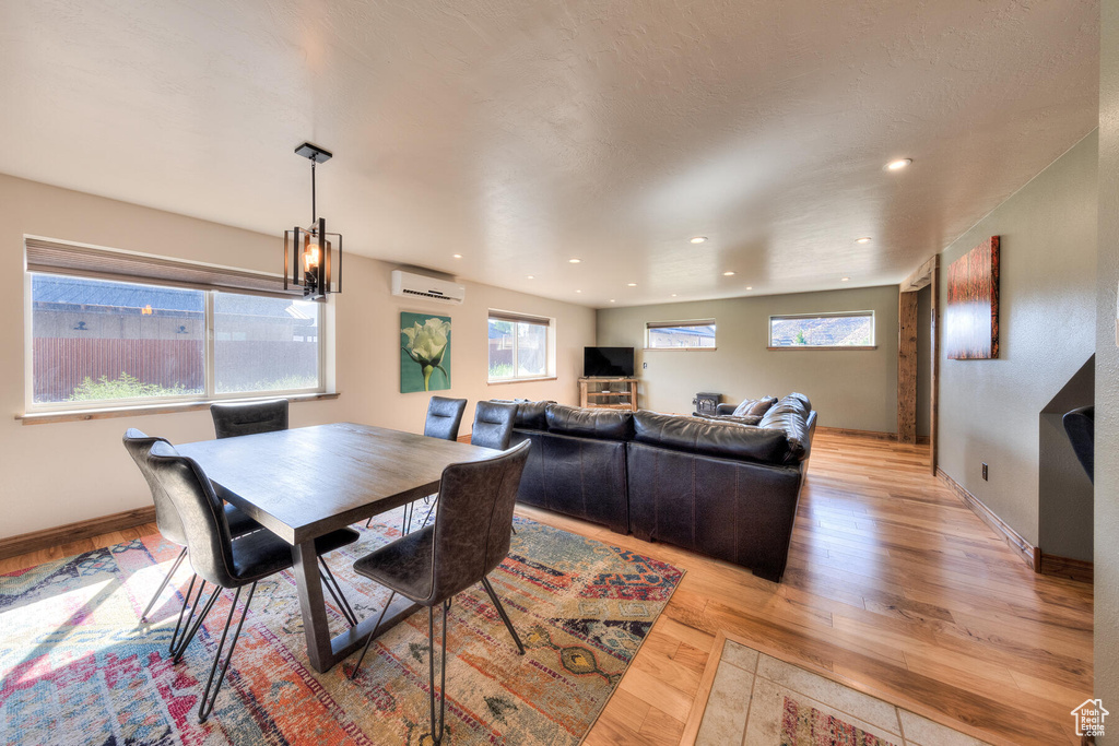 Dining room with an AC wall unit, light hardwood / wood-style floors, and an inviting chandelier