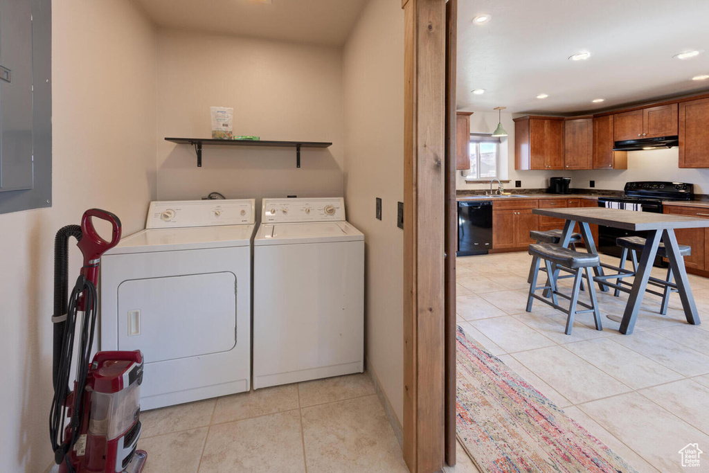 Clothes washing area with light tile patterned floors, electric panel, separate washer and dryer, and sink