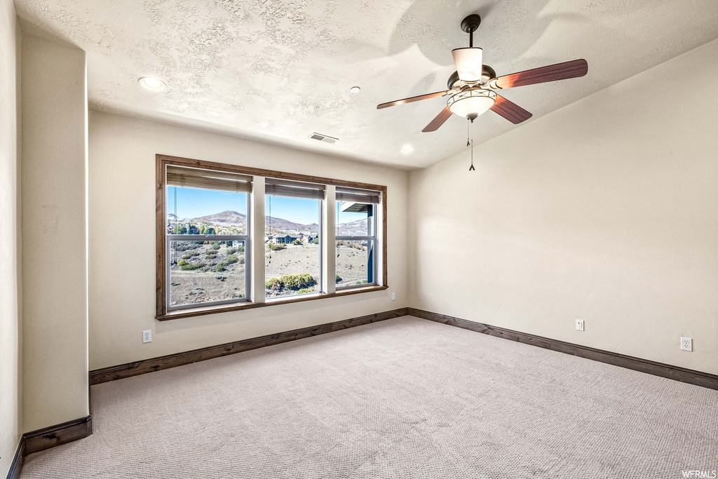 Carpeted empty room with a textured ceiling, lofted ceiling, and ceiling fan