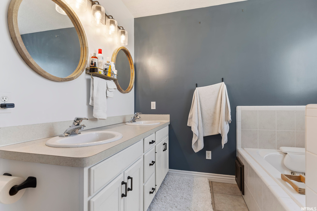 Bathroom with dual vanity, tiled tub, mirror, and light tile floors