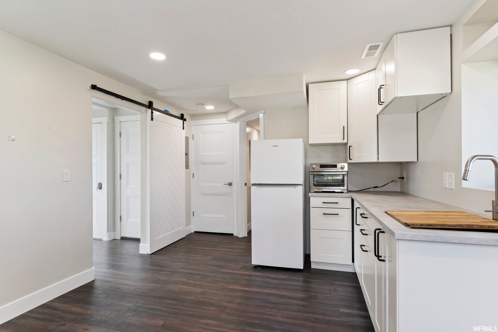 Kitchen with white fridge, white cabinets, light countertops, dark hardwood flooring, and oven