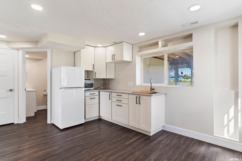 Kitchen featuring dark hardwood flooring, white fridge, light countertops, and white cabinets