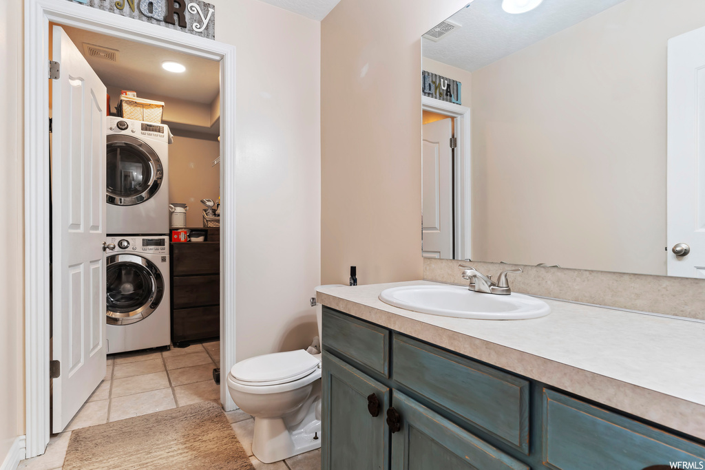 Bathroom featuring vanity, stacked washer / drying machine, mirror, and light tile flooring