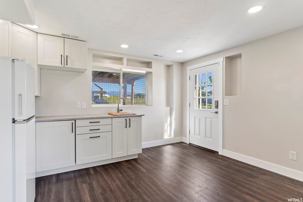 Kitchen with dark hardwood floors, white fridge, light countertops, and white cabinets