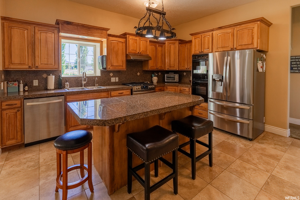 Kitchen featuring stainless steel appliances, a center island, light tile flooring, brown cabinets, and backsplash