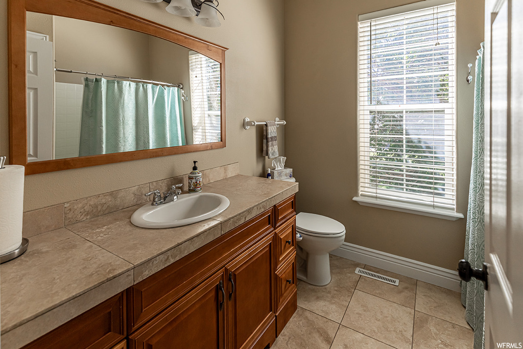 Bathroom with vanity, mirror, a healthy amount of sunlight, and light tile floors