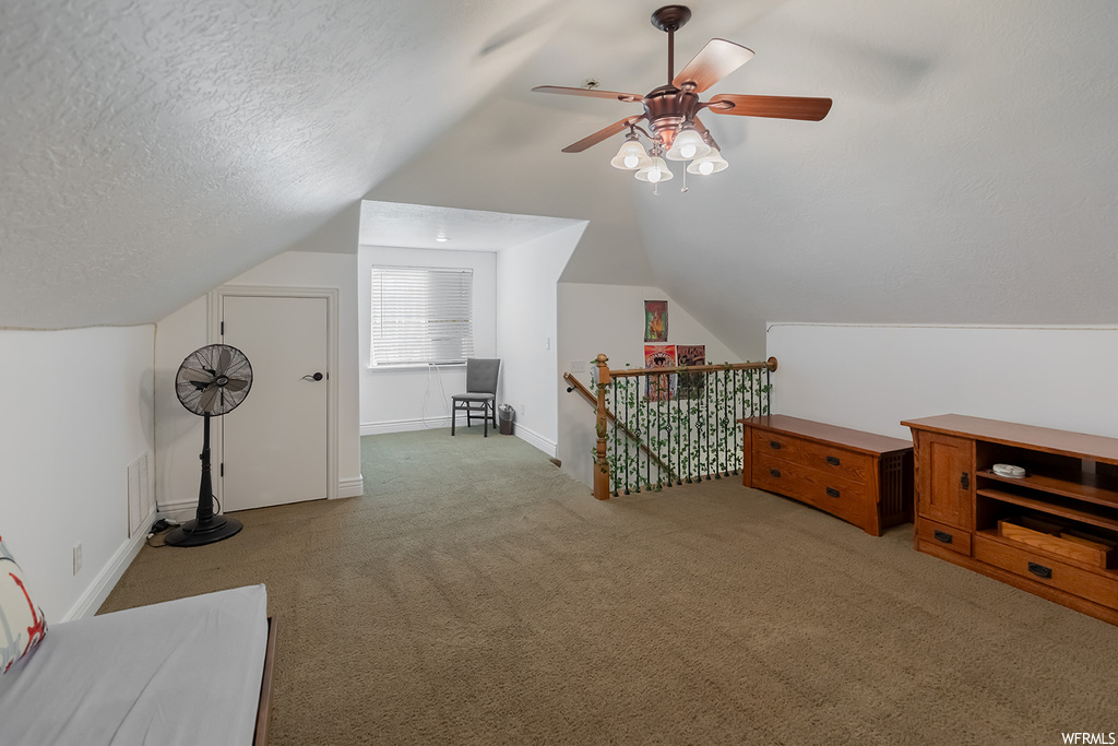 Additional living space featuring a textured ceiling, vaulted ceiling, light carpet, and ceiling fan