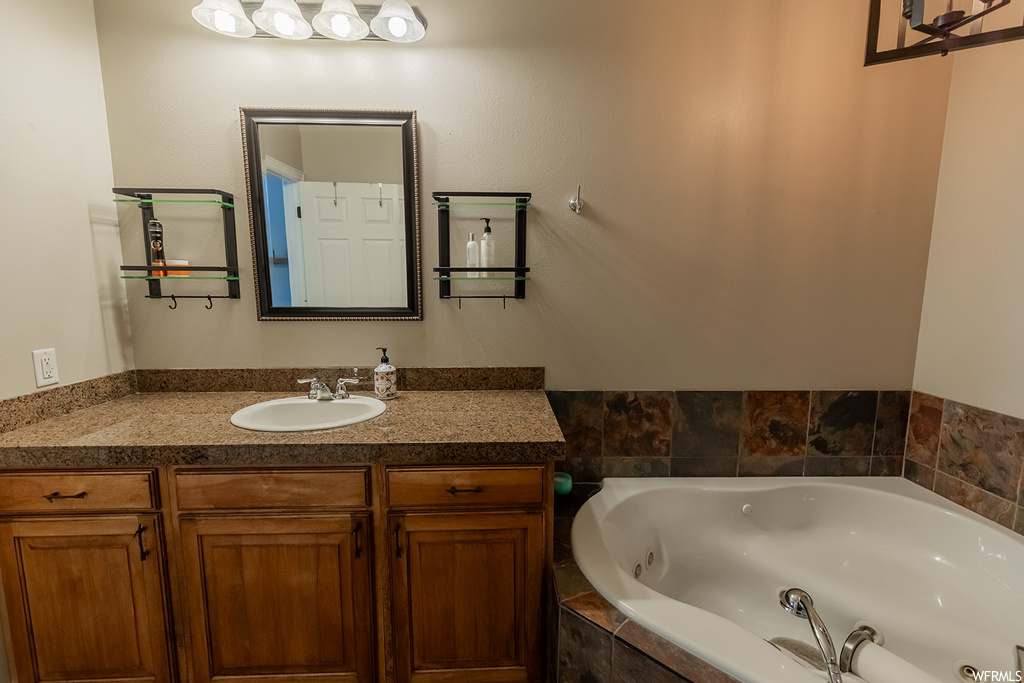 Bathroom featuring tiled tub, mirror, and vanity