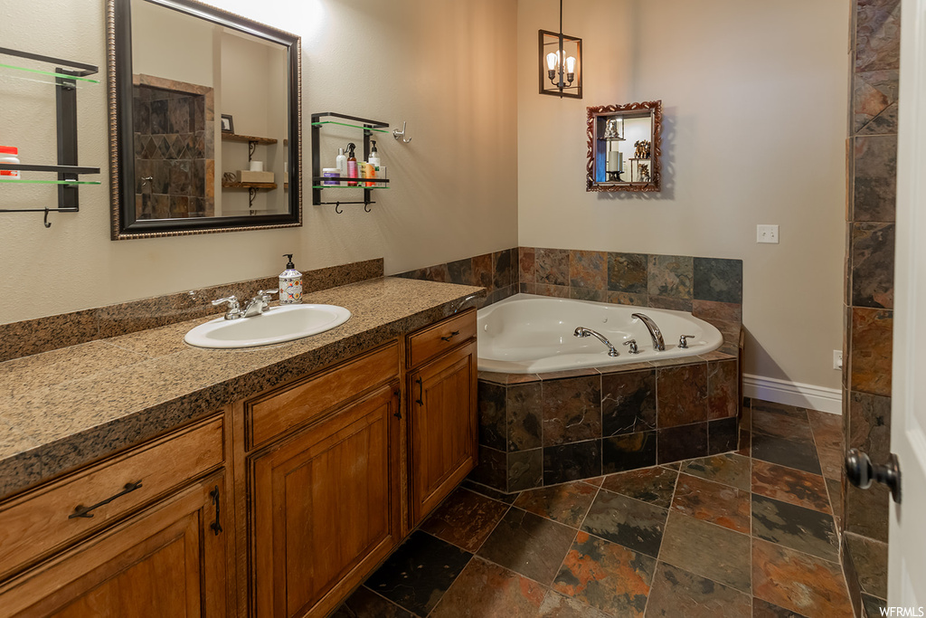 Bathroom featuring dark tile floors, vanity, tiled tub, and mirror