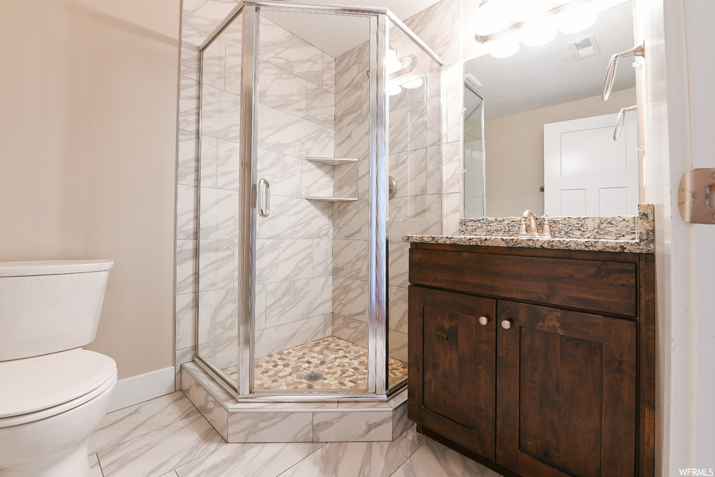 Bathroom with an enclosed shower, vanity, light tile flooring, and mirror