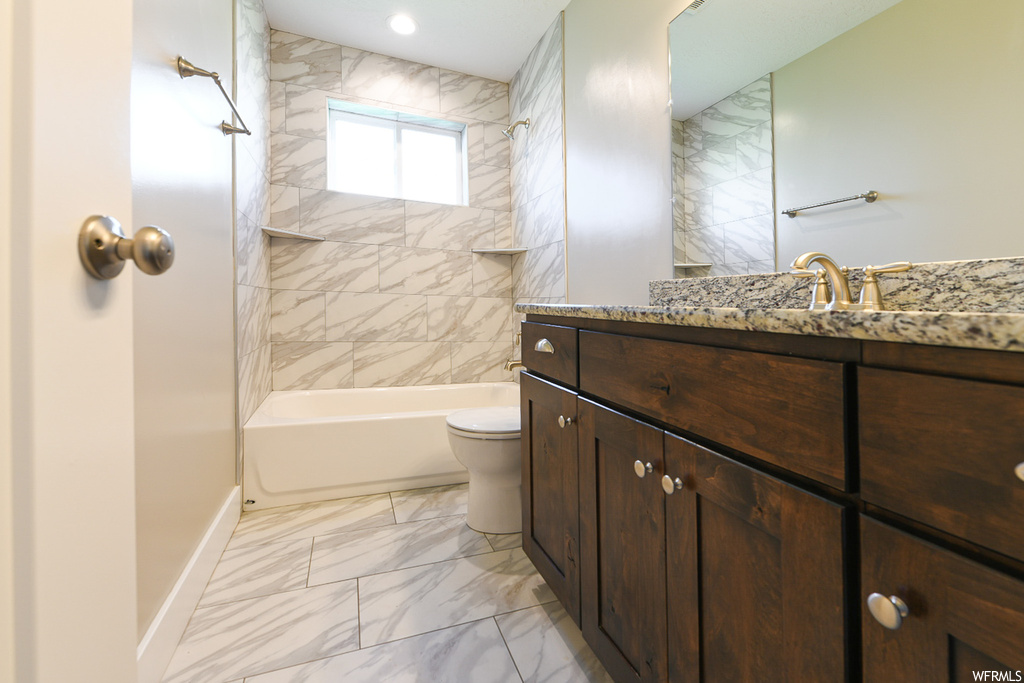 Full bathroom featuring mirror, tiled shower / bath combo, light tile floors, and vanity