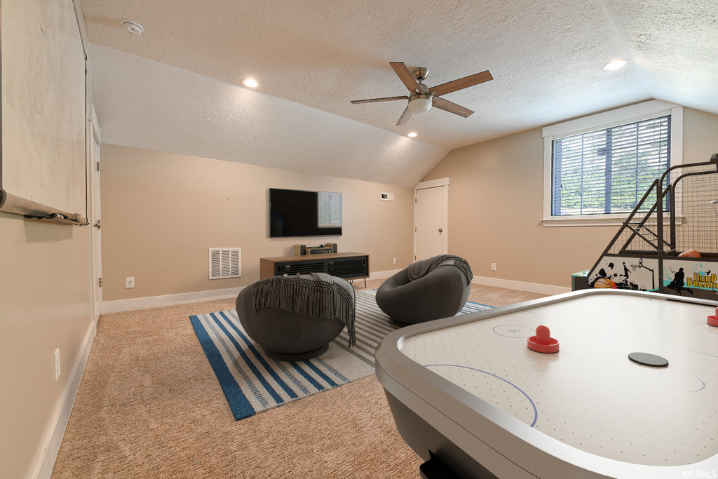 Playroom with a textured ceiling, vaulted ceiling, light carpet, and ceiling fan
