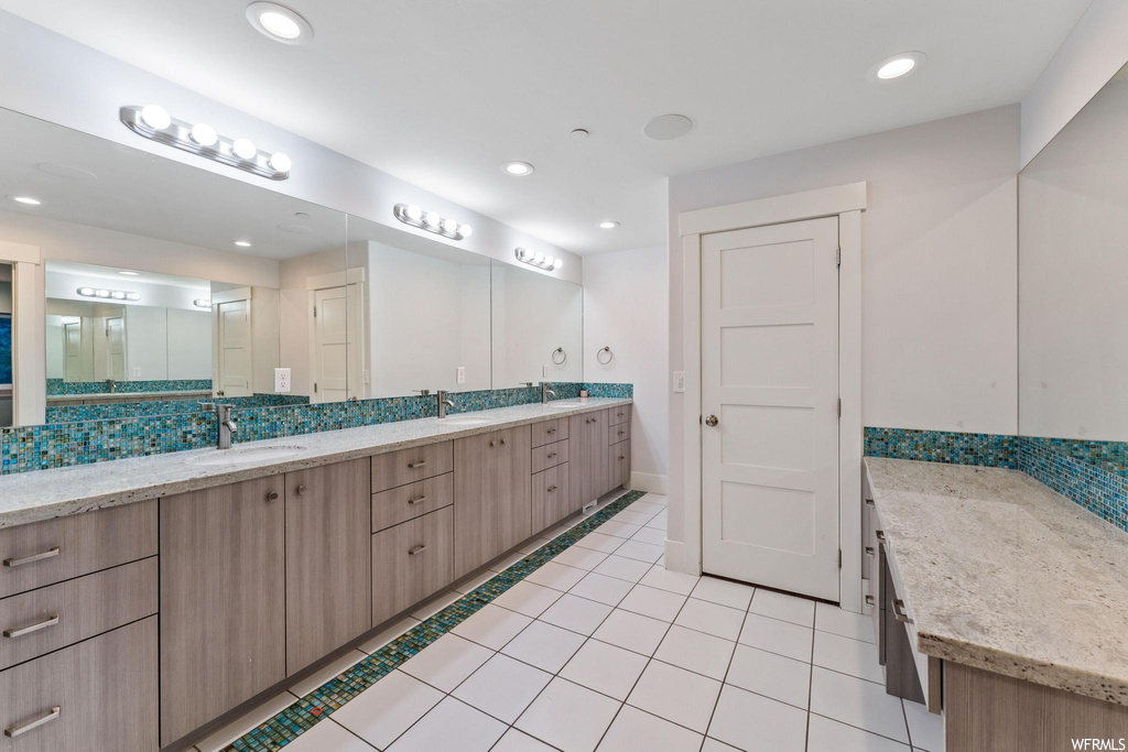 Bathroom with dual bowl vanity, mirror, and light tile floors