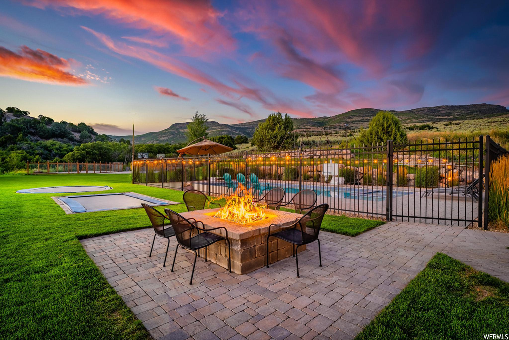 Patio terrace at dusk with a lawn, pool, a firepit, and a mountain view