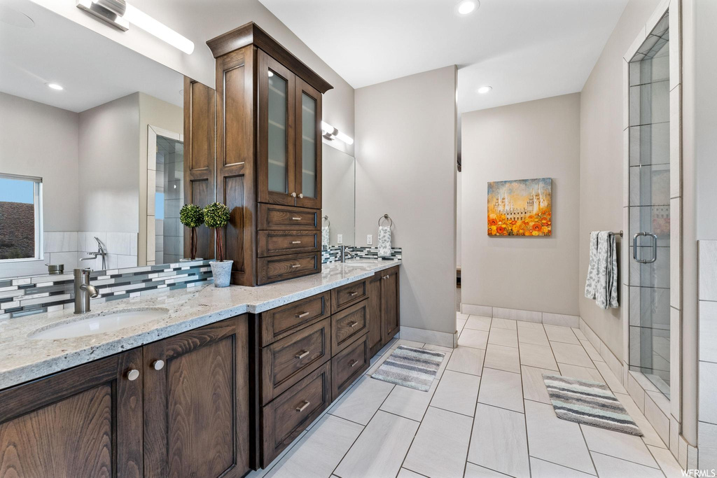 Bathroom with a shower with door, light tile flooring, mirror, double large sink vanity, and backsplash