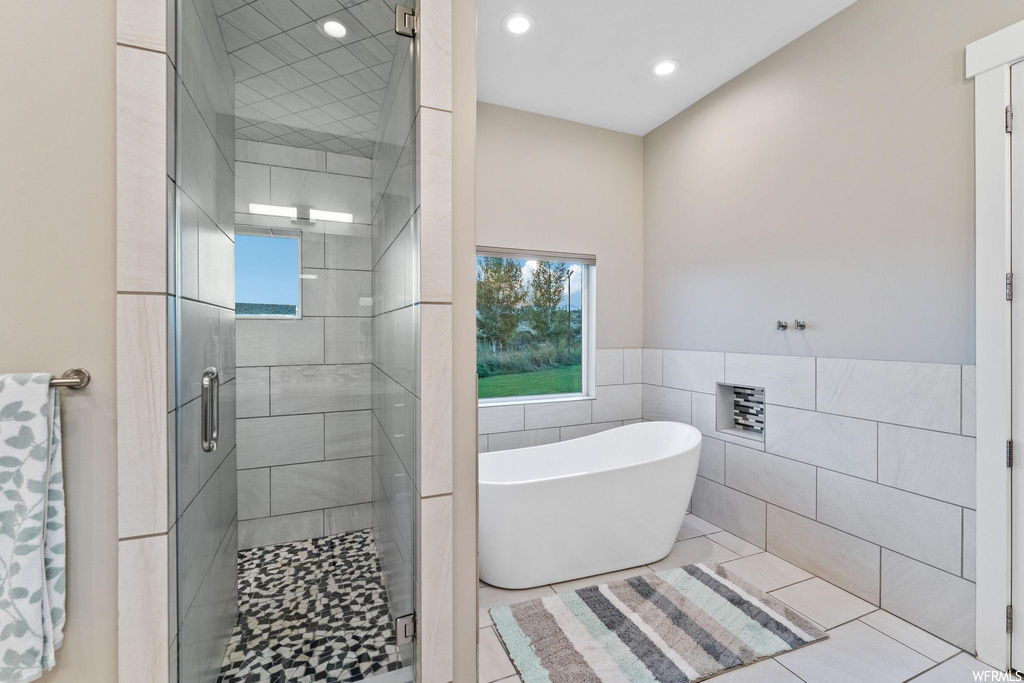 Bathroom featuring separate shower and tub, tile walls, and light tile floors