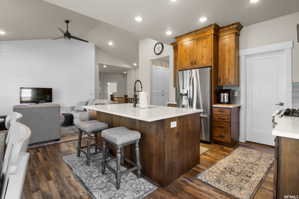 Kitchen featuring dark hardwood floors, vaulted ceiling, light countertops, a kitchen island, stainless steel refrigerator with ice dispenser, and a high ceiling