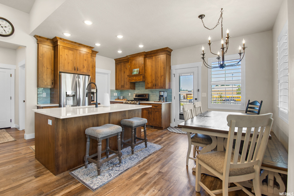 Kitchen featuring a notable chandelier, a center island, stainless steel refrigerator with ice dispenser, range, brown cabinets, light countertops, backsplash, and light hardwood floors