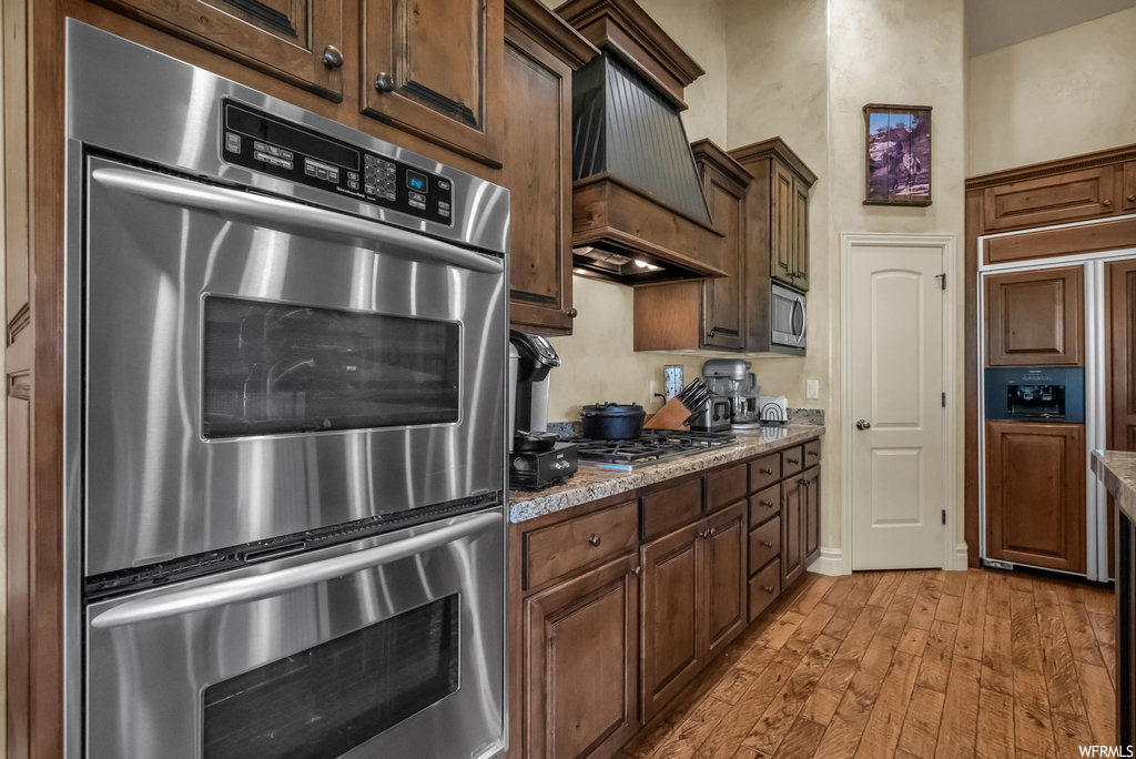 Kitchen featuring light hardwood flooring, stone countertops, built in appliances, and custom exhaust hood