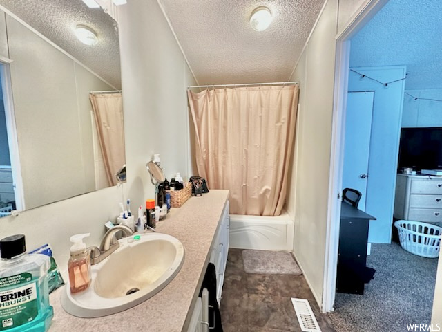 Bathroom with a textured ceiling, vanity with extensive cabinet space, mirror, shower / bath combo with shower curtain, and dark tile floors
