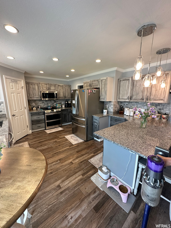 Kitchen with appliances with stainless steel finishes, a center island, pendant lighting, stone counters, dark hardwood flooring, ornamental molding, and backsplash