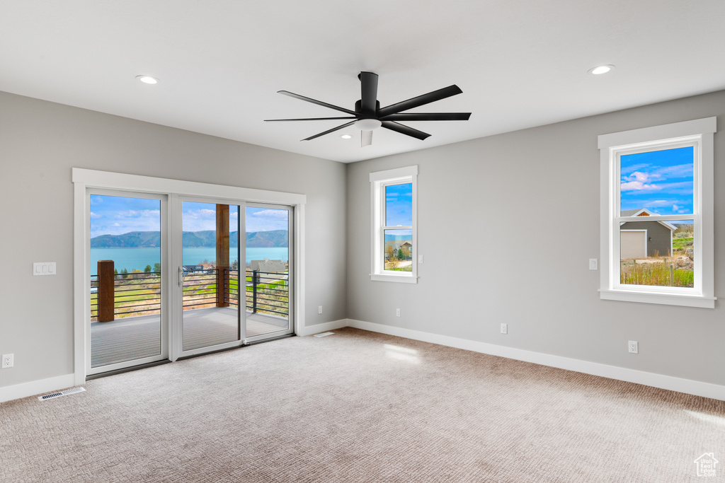 Carpeted empty room featuring plenty of natural light, ceiling fan, and a water view