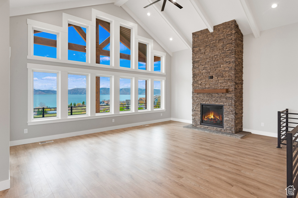 Unfurnished living room with high vaulted ceiling, light hardwood / wood-style floors, a fireplace, and a water view