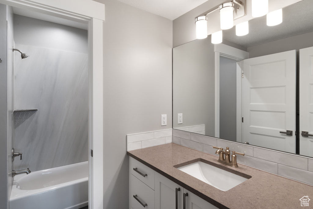 Bathroom with backsplash, vanity with extensive cabinet space, and shower / washtub combination