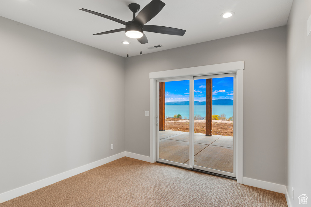 Carpeted empty room featuring a water view and ceiling fan
