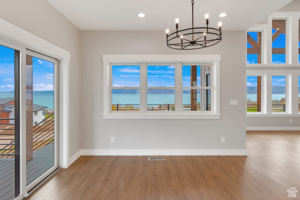 Unfurnished dining area with hardwood / wood-style floors, a water view, and a chandelier