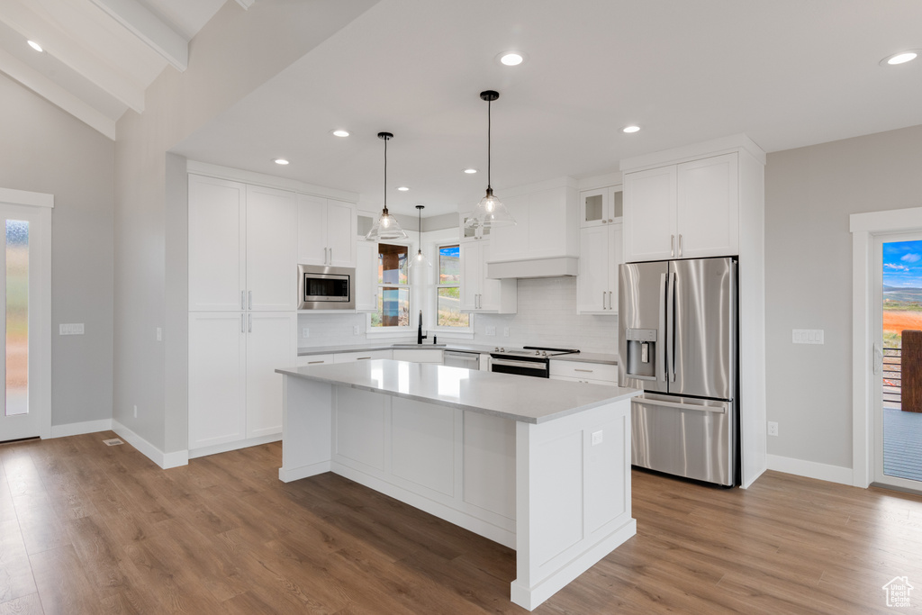 Kitchen featuring appliances with stainless steel finishes, hardwood / wood-style flooring, white cabinets, backsplash, and vaulted ceiling