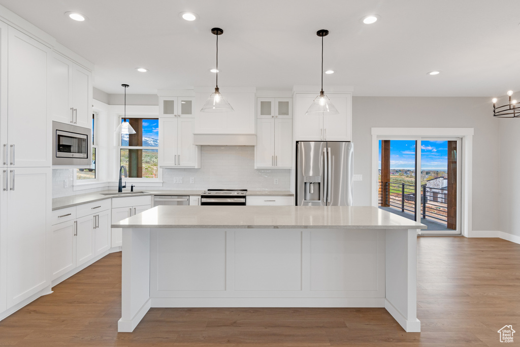 Kitchen featuring light hardwood / wood-style floors, a kitchen island, backsplash, white cabinetry, and appliances with stainless steel finishes