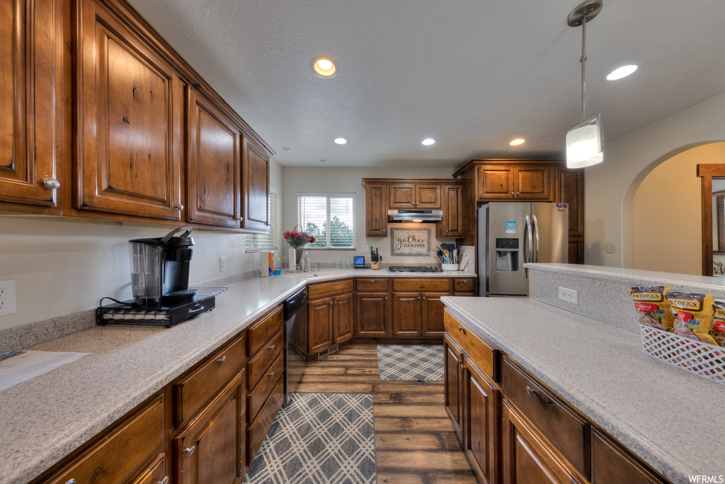 Kitchen featuring appliances with stainless steel finishes, pendant lighting, light stone counters, hardwood flooring, and brown cabinets