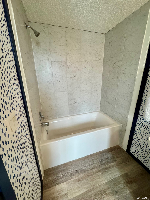 Bathroom featuring a textured ceiling, shower / washtub combination, and wood-type flooring