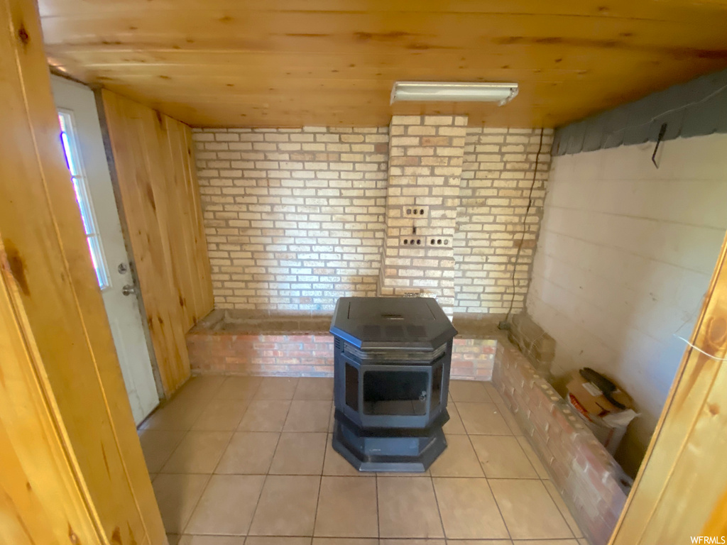 Bathroom with brick wall, light tile flooring, and wooden ceiling