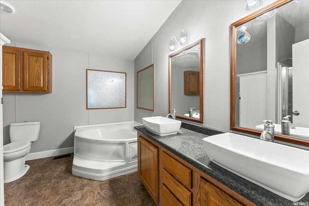 Bathroom with dark tile floors, double large vanity, mirror, and a bath to relax in