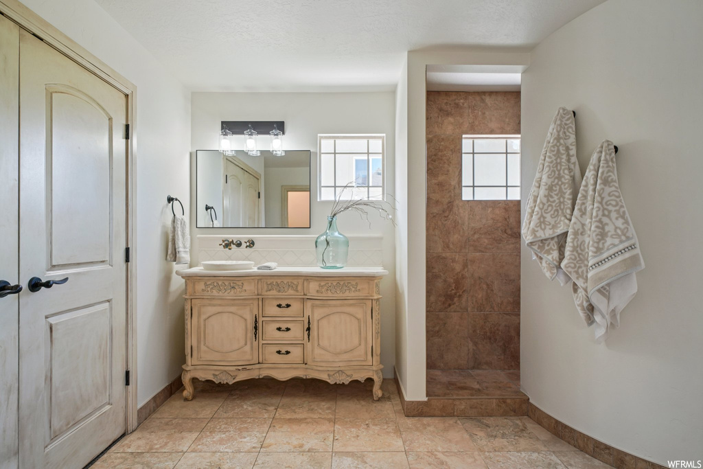 Bathroom featuring light tile floors, mirror, and dual vanity