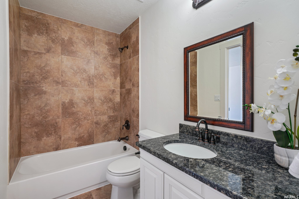 Full bathroom featuring a textured ceiling, oversized vanity, tiled shower / bath, and mirror