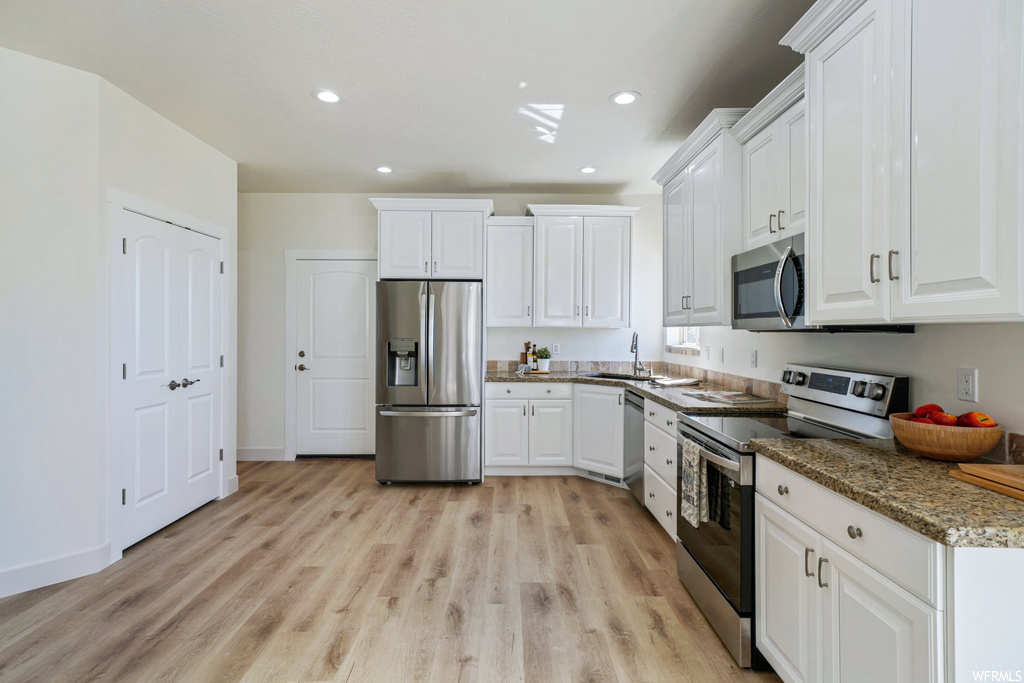 Kitchen with stainless steel appliances, white cabinetry, and light hardwood flooring