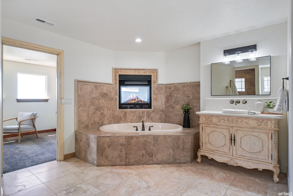 Bathroom with vanity with extensive cabinet space, tiled tub, mirror, and light tile floors