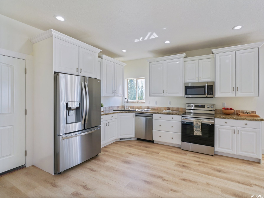 Kitchen featuring white cabinets, light hardwood floors, and stainless steel appliances