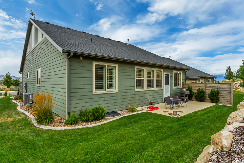 Back of property with a lawn, a patio area, and central AC unit