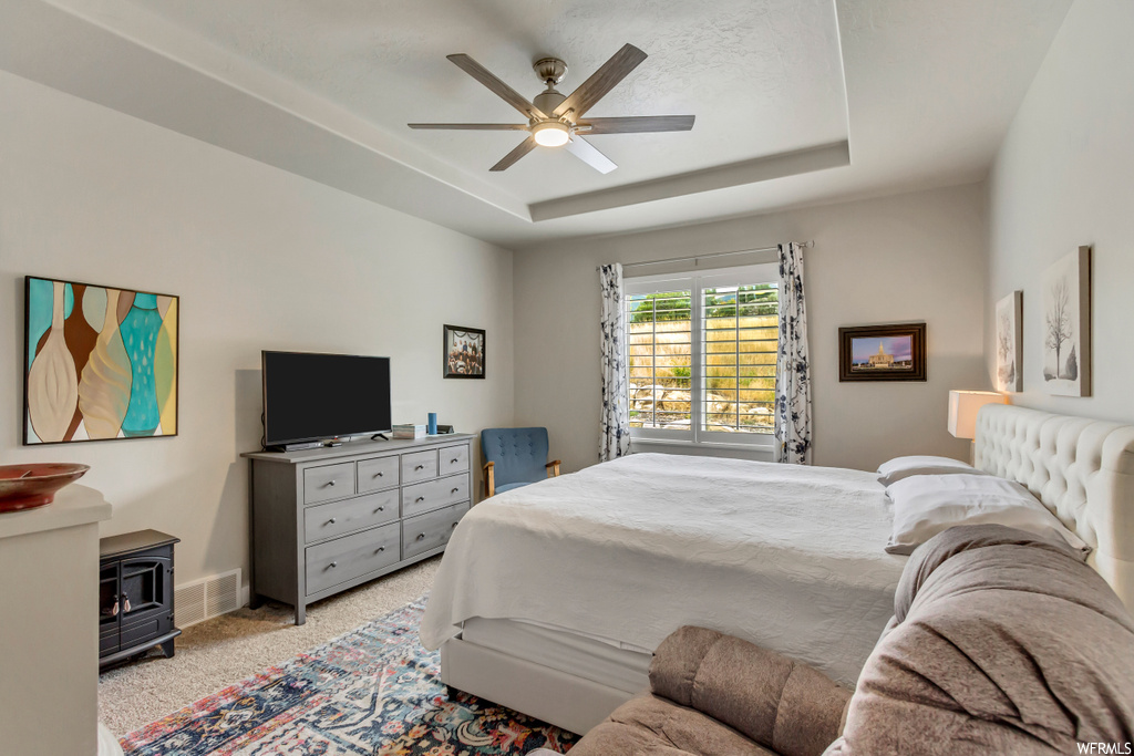 Bedroom featuring a tray ceiling, light carpet, and ceiling fan