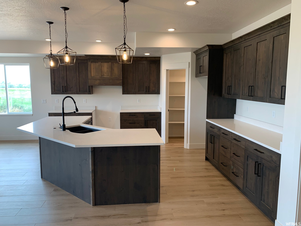 Kitchen with pendant lighting, light hardwood flooring, dark brown cabinets, and light countertops