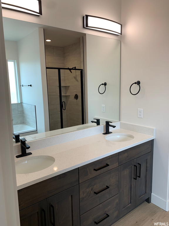 Bathroom featuring separate shower and tub, double sink vanity, light hardwood floors, and mirror